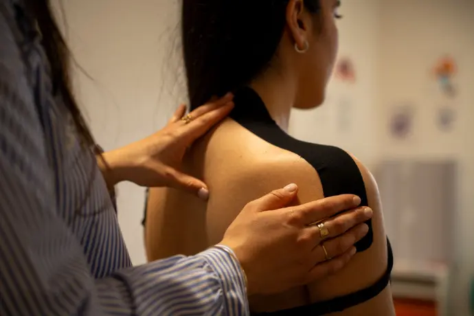 Application de taping chiropratique sur l’épaule d’une patiente